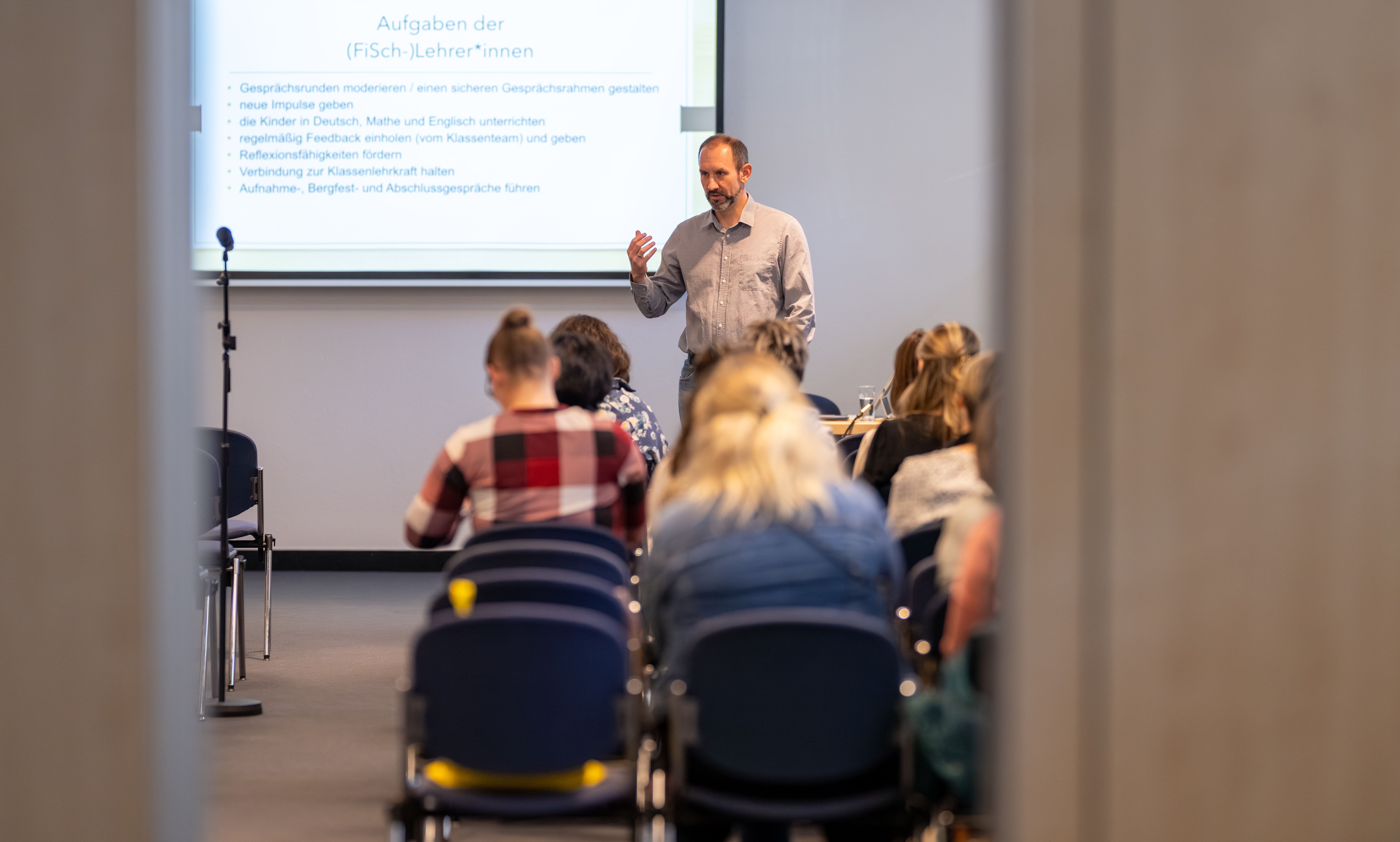 Lehrkräfte sitzen in Stuhlreihen und hören einem Referenten bei einem Workshop zu
