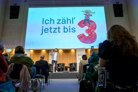 Raphael Kirsch steht auf der Bühne, auf der Folie im Hintergrund steht groß "Ich zähl jetzt bis 3"
