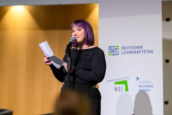 Eine Frau steht mit einem Blatt Papier in der Hand auf der Bühne und macht Poetry Slam