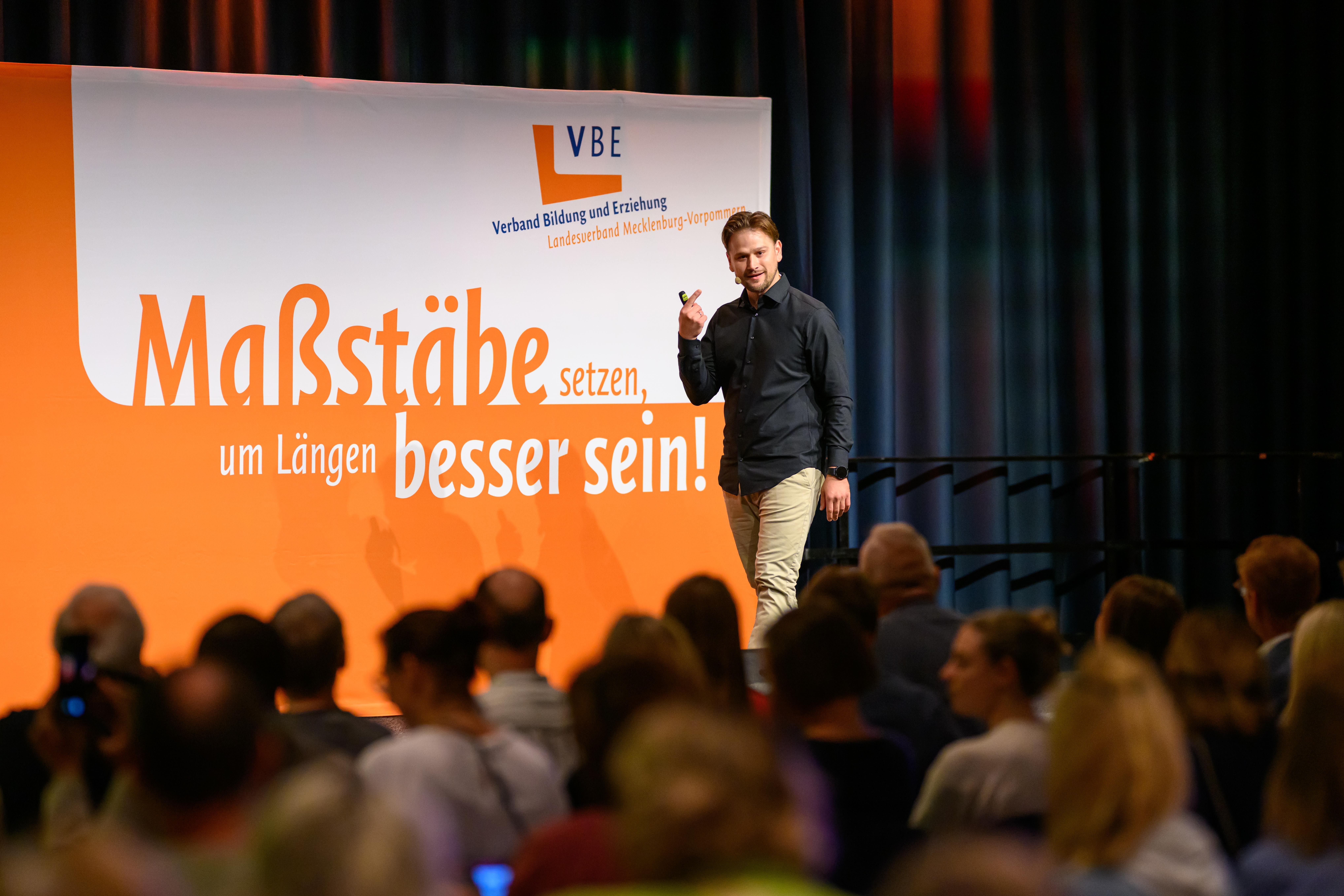 Örs Turoczy steht auf einer Bühne und spricht zum Publikum.